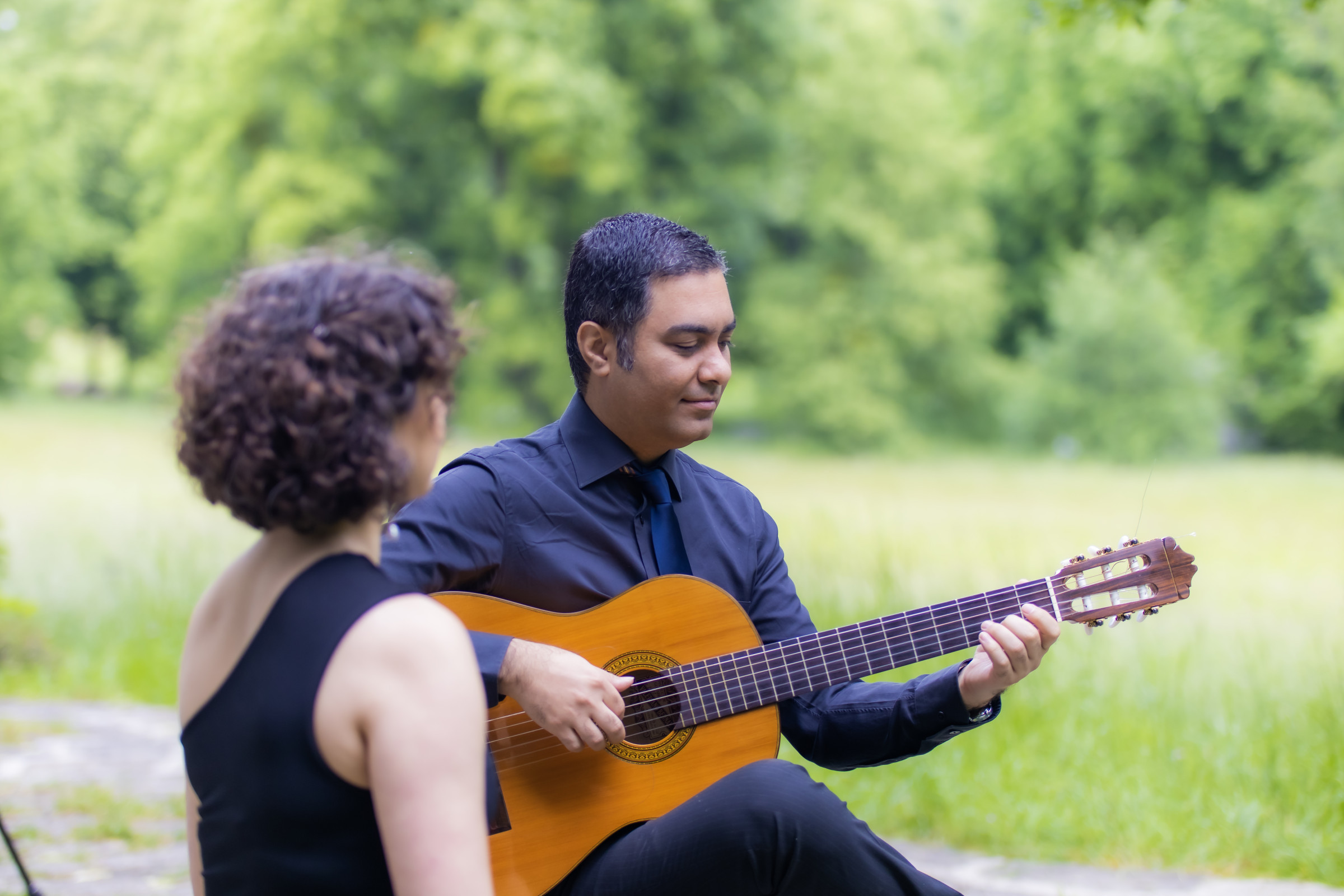 Two people outdoors, one playing an acoustic guitar