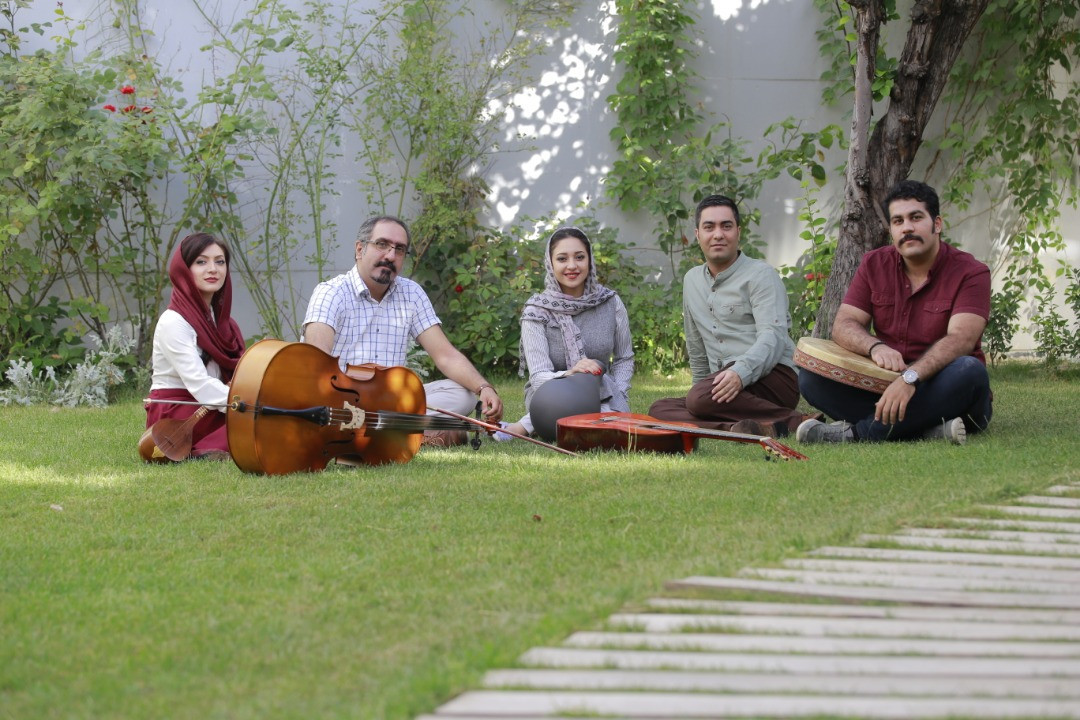 Five musicians seated on grass with their instruments
