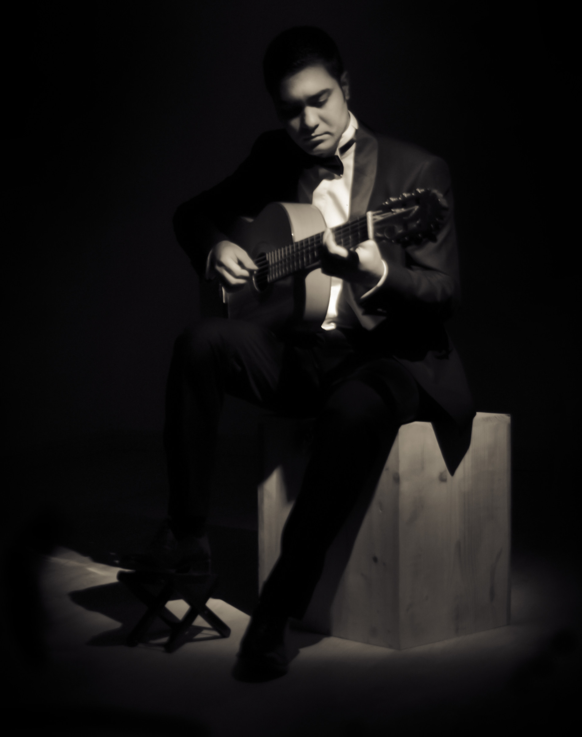A seated acoustic guitarist in a dark monochrome portrait