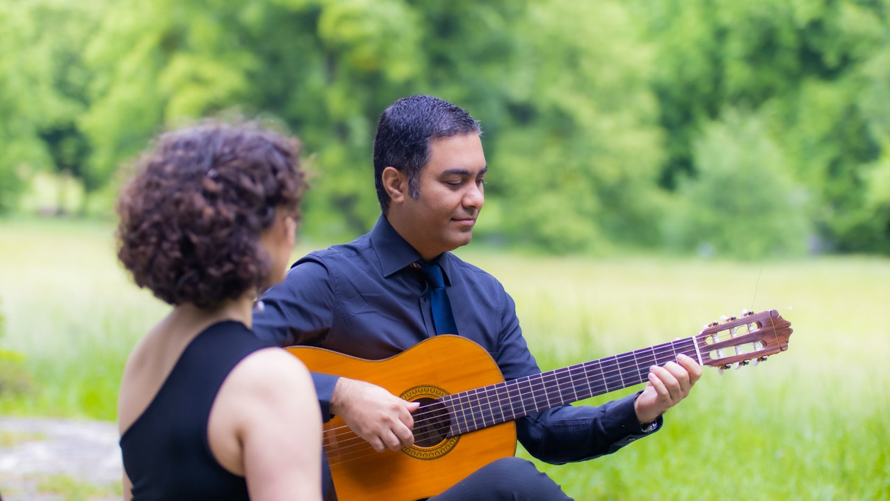Two people outdoors, one playing an acoustic guitar